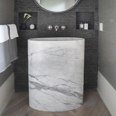 a white marble sink in a bathroom under a round mirror with black and grey walls