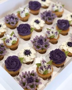 cupcakes decorated with purple and white flowers in a box