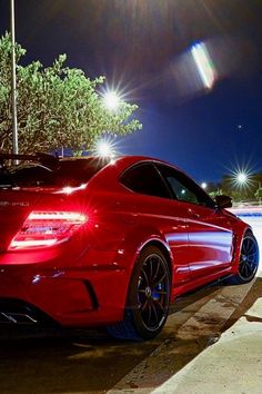 a red sports car parked in front of a parking meter at night with the lights on