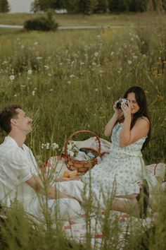 a man and woman are sitting in the grass talking on their cell phones while eating food