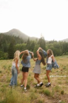 four girls are standing in a field with their arms around each other and one girl is holding her head