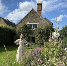 a woman standing in the middle of a garden next to a house with flowers on it