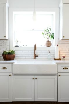 a kitchen with white cabinets and a window above the sink that has plants in it