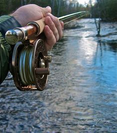 a man holding onto a fishing rod with a river in the background