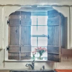 a kitchen sink sitting under a window with shutters on the windowsill and flowers in a vase