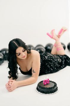 a woman laying on the floor next to a black cake with pink candles in it