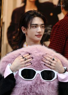 a person with sunglasses on their face holding up a pink fur coat and wearing black rings