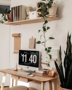 a desk with a computer on top of it next to a potted plant and bookshelf