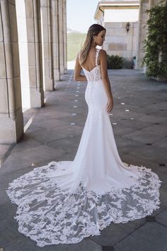 a woman in a white wedding dress is standing on the sidewalk with her back to the camera