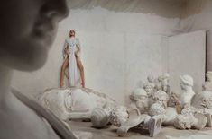 a woman standing on top of a pile of white sculptures in a room filled with plaster busturines