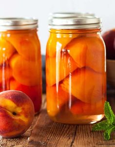 two jars filled with peaches on top of a wooden table