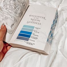 a person holding an open book on top of a white sheet covered bed with the title daughter of the moon goddess