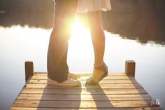 two people standing on a dock with the sun shining through their pants and shoes in front of them