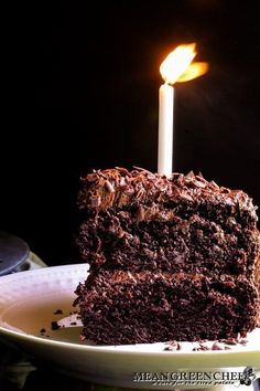 a slice of chocolate cake on a plate with a lit candle in the middle,