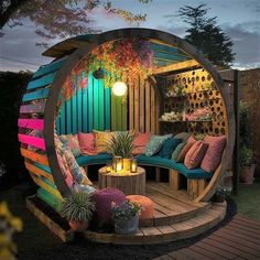 an outdoor seating area with colorful pillows and lights on the outside, surrounded by wood planks