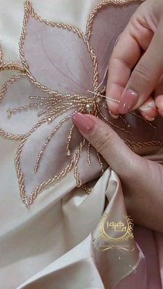 a woman's hands are working on something with gold thread and beads in her left hand