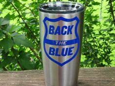 a stainless steel tumbler with the words back the blue on it sitting on a wooden table