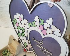 a heart shaped sign with flowers and hearts on it, in front of a wooden box