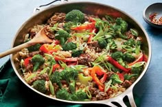 a skillet with broccoli, carrots and rice in it on a blue surface