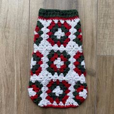 a crocheted red, white and green afghan on a wooden floor with wood floors