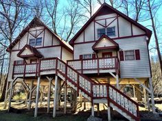 two story house with red trim and white railings on the front, surrounded by trees