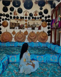 a woman sitting on top of a bed in a room filled with lots of plates