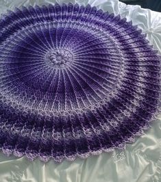 a purple crocheted doily sitting on top of a white bed sheet in the shape of a circle