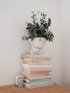 a stack of books sitting on top of a table next to a vase filled with plants