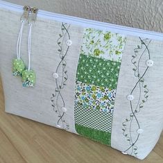 a white zippered bag with green and white patchwork designs on it, sitting on a wooden table