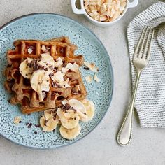 a plate topped with waffles covered in banana slices and nuts next to a cup of coffee