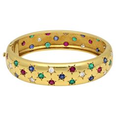 A vintage multi colour gemstone and yellow gold bangle bracelet by Cartier Paris, circa 1990. The 18ct yellow gold bangle has a rounded profile with a combination of diamonds, rubies, sapphires and emeralds all the way around, each in a five point star setting. The bangle is hinged to the side and secured with a concealed tongue and box clasp and safety catch. Maker Cartier Period circa 1980/90s Origin Paris Gemstones 12 x round brilliant cut diamonds - estimated 1.20ct 12 x sapphires - estimate Vintage Cartier Watch, Five Point Star, Star Setting, Cartier Vintage, Yellow Gold Bangle, Vintage Bangles, Vintage Star, Box Clasp, Gold Bangle Bracelet