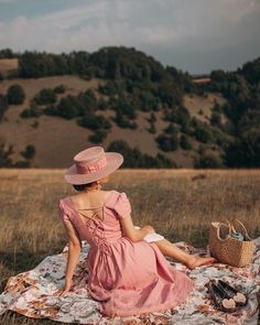 a woman in a pink dress and hat sitting on a blanket