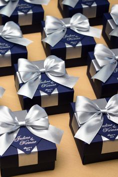 many small boxes with bows on them are sitting on a table together, one is blue and the other is silver