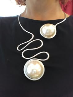 a woman wearing a black shirt and white necklace with two large pearls on the front