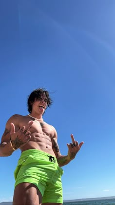 a shirtless man standing on the beach with his hands in the air and one hand out