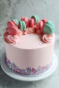 a pink frosted cake with macaroons and sprinkles on top