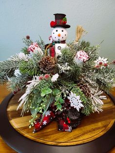 a wooden table topped with a snowman and pine cone centerpiece filled with greenery