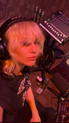 a woman with headphones on sitting in front of a microphone and mixing equipment at a recording studio