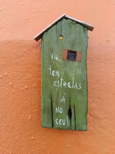 a green birdhouse with graffiti written on it's side against a pink wall