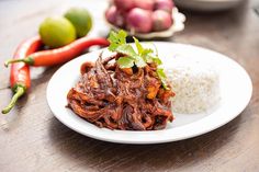 a white plate topped with meat and rice next to vegetables on a wooden counter top