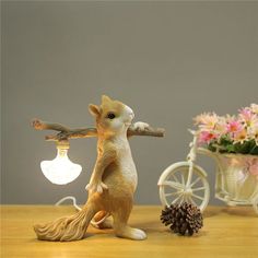 a squirrel figurine holding a light bulb on top of a table next to flowers