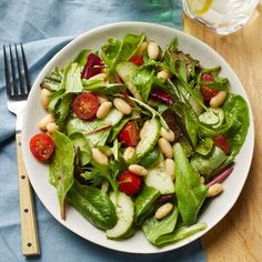 a white plate topped with spinach salad next to a fork and glass of water