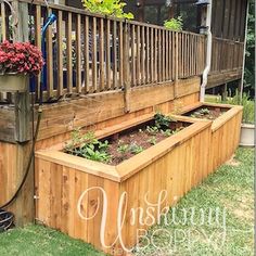 a wooden planter box filled with plants on top of a grass covered yard next to a fence