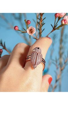 a woman's hand with a ring on it and some flowers in the background