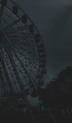 a large ferris wheel sitting next to a dark cloud filled sky with the moon in the distance