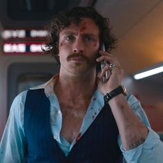 a man with a moustache talking on a cell phone while wearing a vest