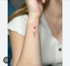 a woman's wrist with a small pink flower tattoo on the left side of her arm