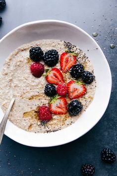 a bowl of oatmeal with strawberries and blackberries on the side