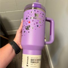 a person holding up a purple tumbler with stars on the side and pink lid