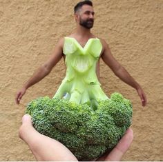 a man in a dress made out of broccoli is standing next to a wall